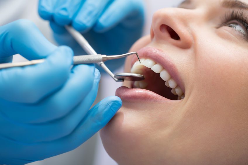 Close-up of a dental check-up, with a dentist wearing blue gloves using dental instruments to examine a patient's teeth.